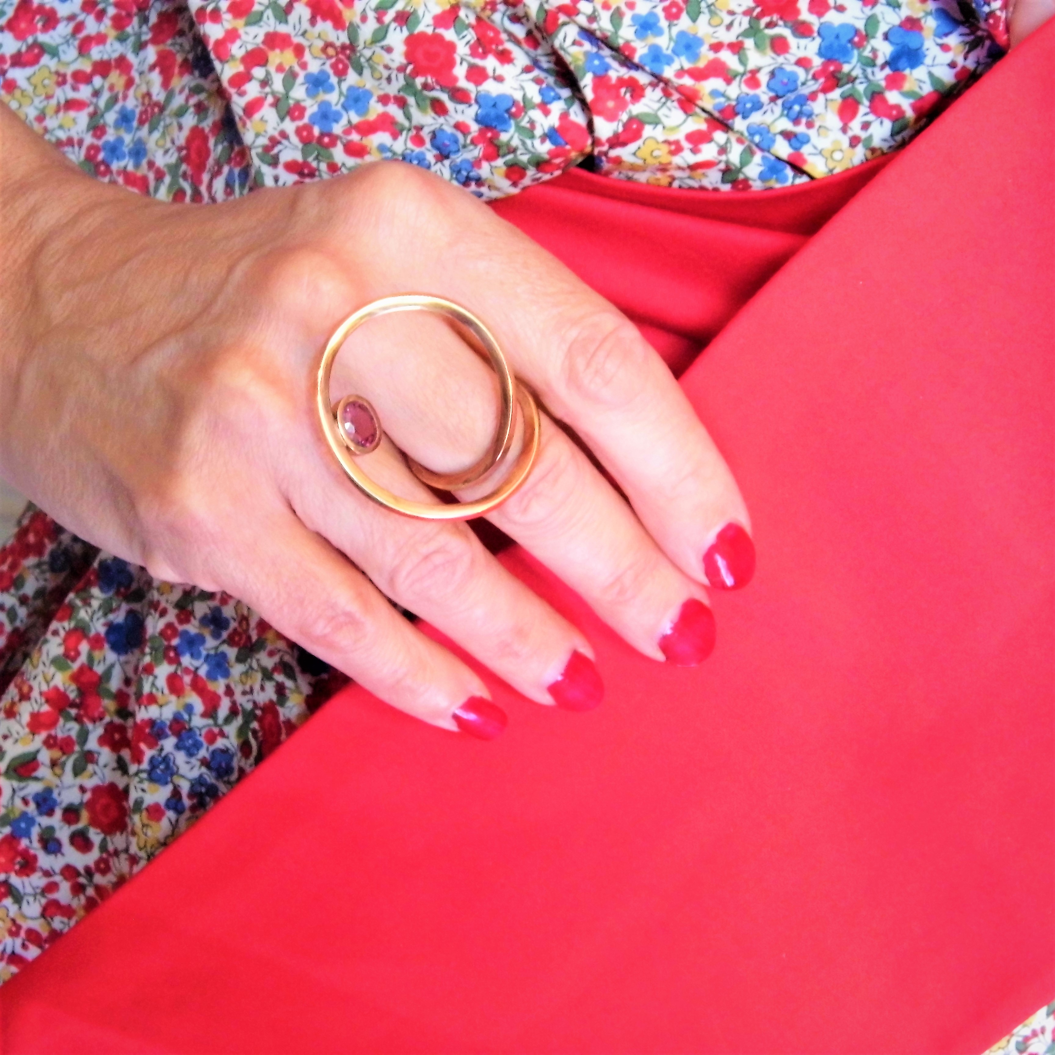 L'image représente un bijou, c'est une bague originale sertie avec un Rubis. Le décor est composé de tissus liberty avec une teinte rouge.